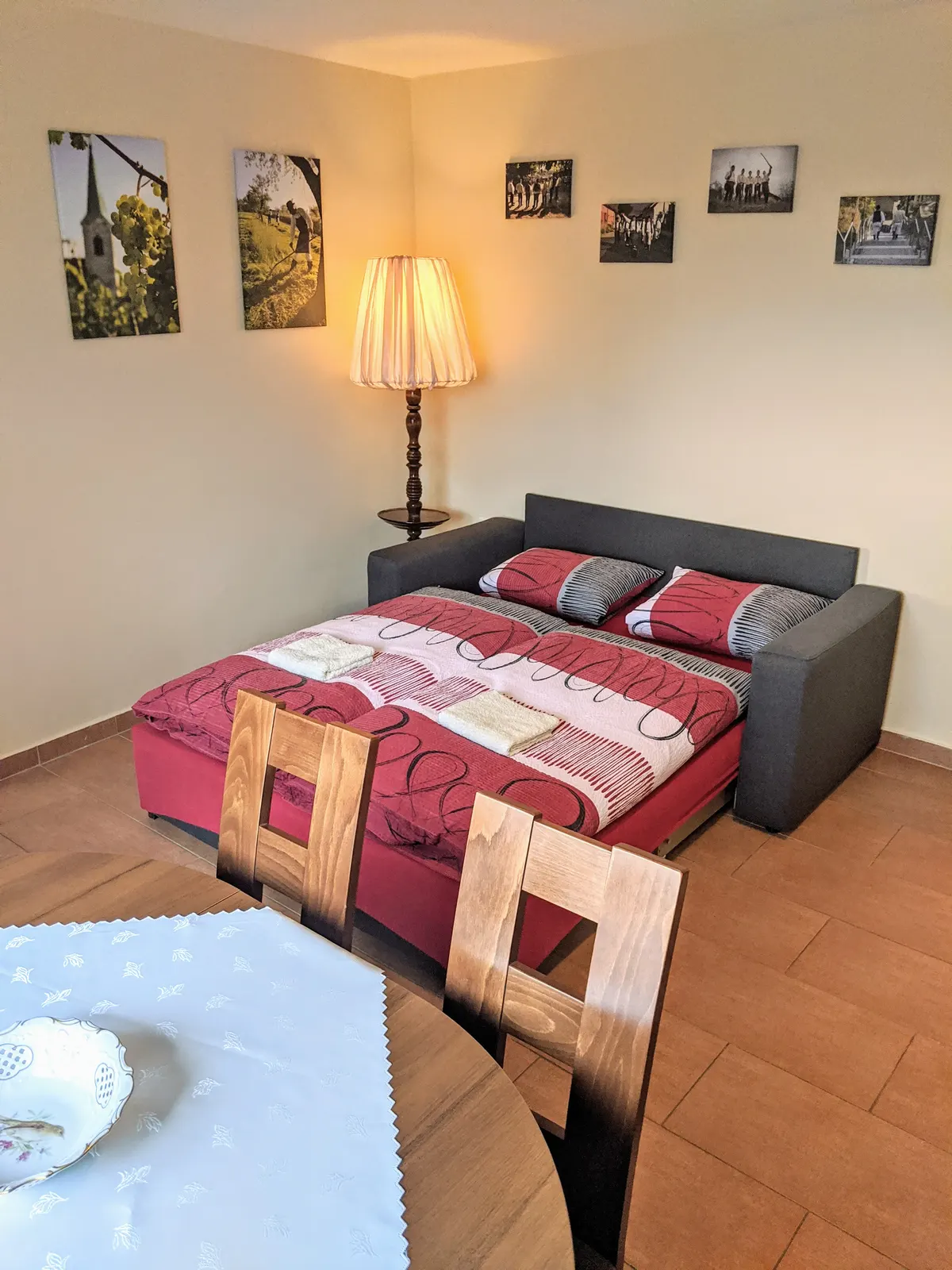 Rozložená pohovka v Apartmánu, ustlaná pro dva, vedle stojací lampy a jídelního stolu